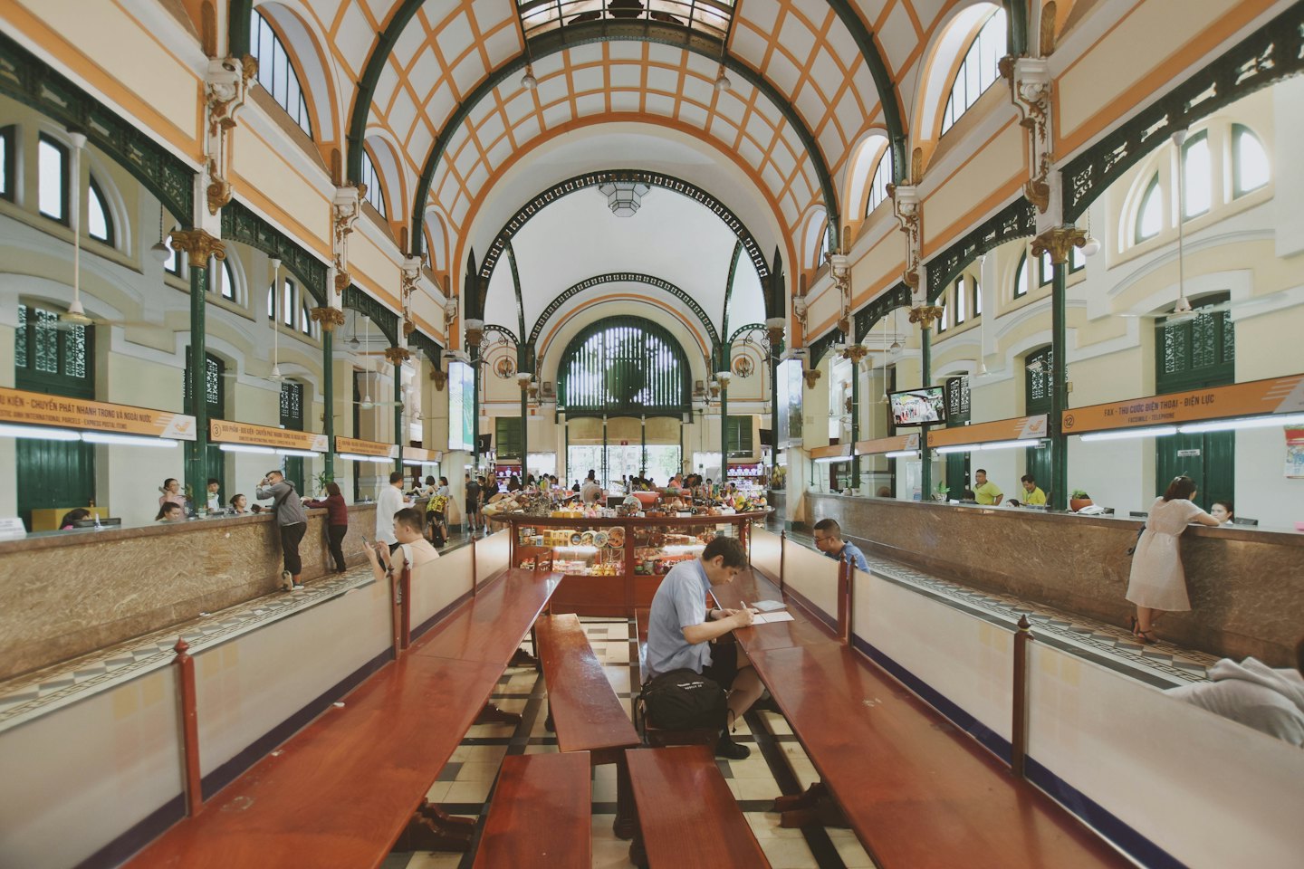 People fill out forms at desks in a grand public hall.