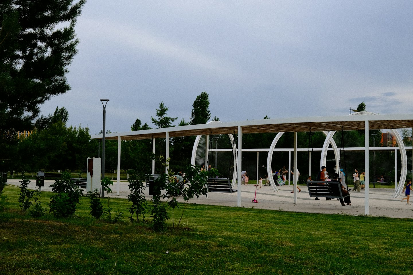 People enjoy the modern park with wooden pergolas and swings.