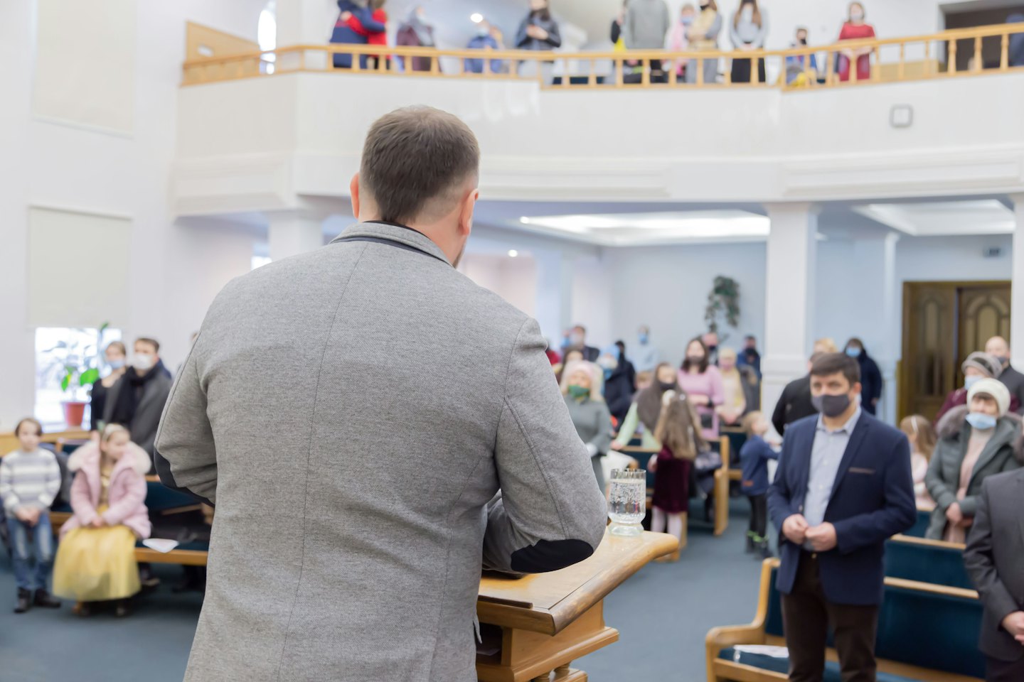 Man speaking at lectern to diverse group in hall.